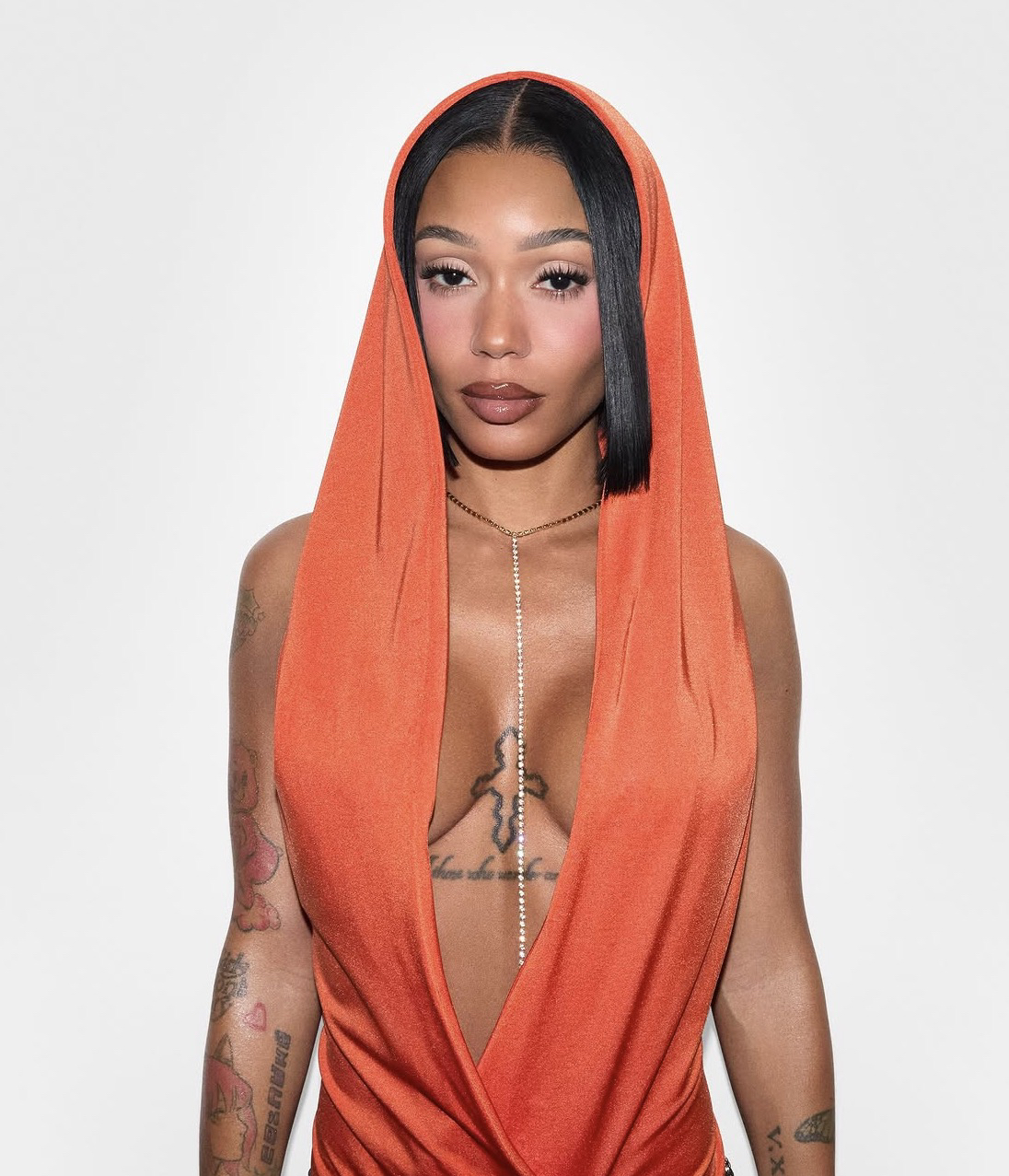 Retrato de estudio de Coi Leray con un vestido naranja con capucha, sobre un fondo blanco liso