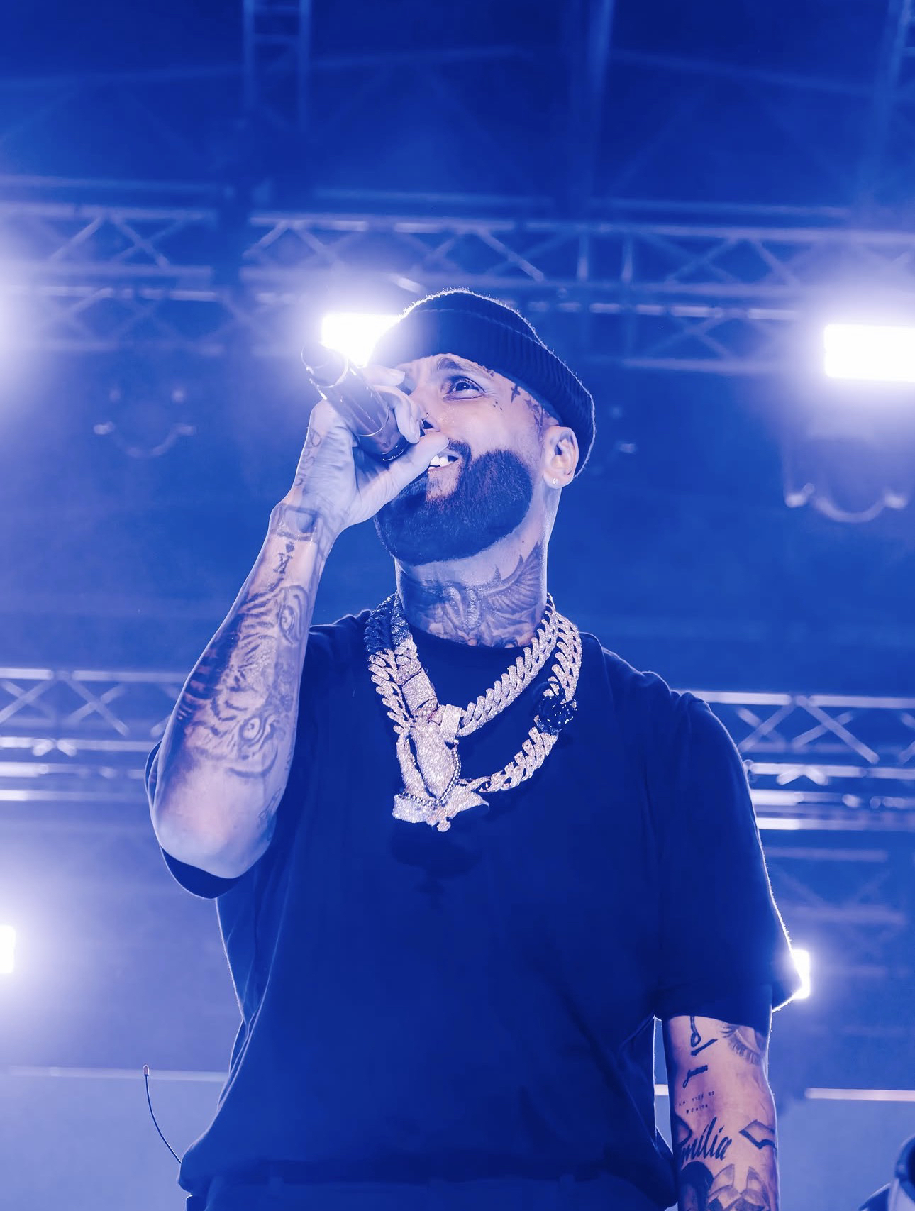 Nicky Jam en concierto, micrófono en mano, bajo luces de escenario azules
