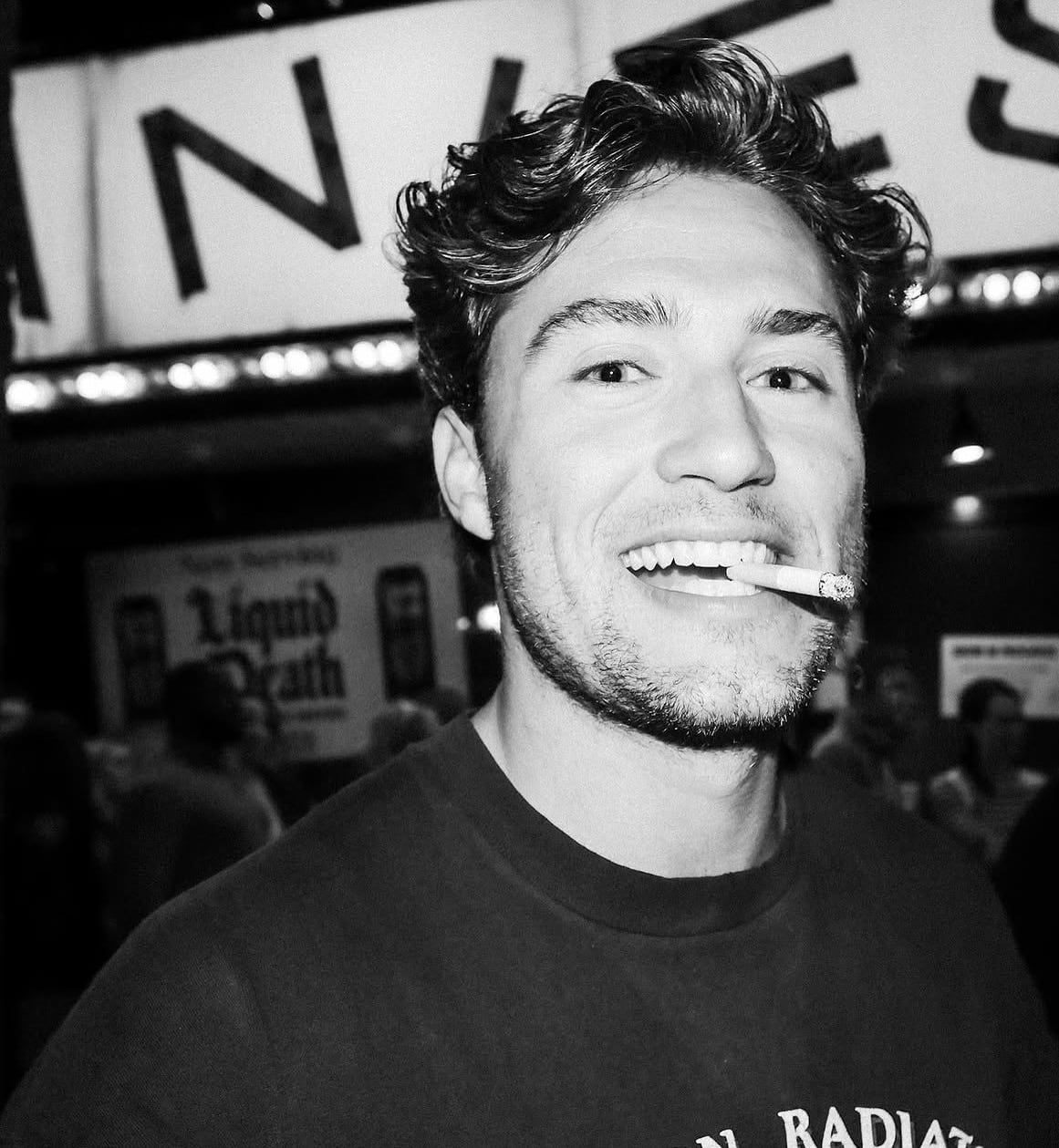 Retrato en blanco y negro de Alec Flynn sonriendo frente a la marquesina de Zanies.
