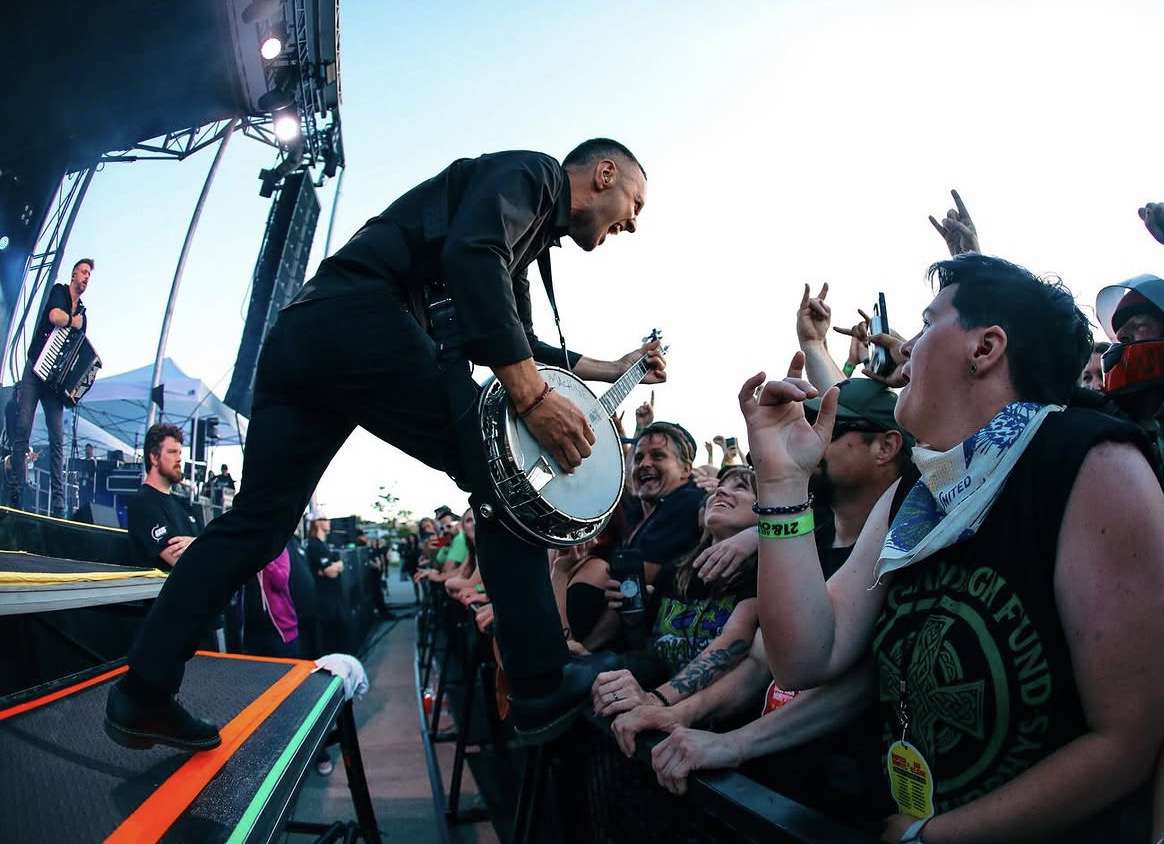 Músico de Dropkick Murphys tocando el banjo, inclinado hacia el público en un show al aire libre