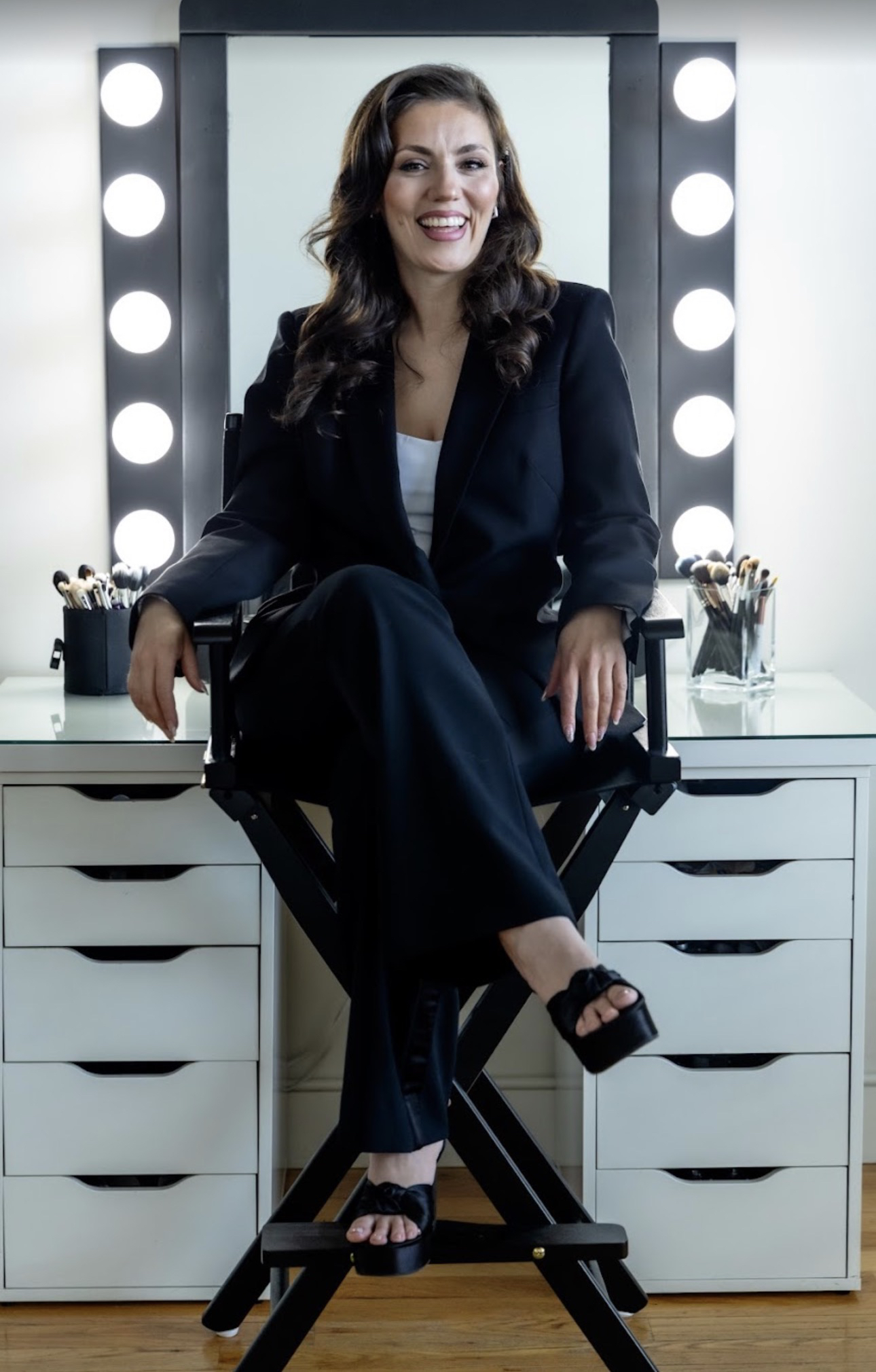 Barbara Rodriguez sonriendo, sentada en una silla de maquillista en su estudio de Lowell.