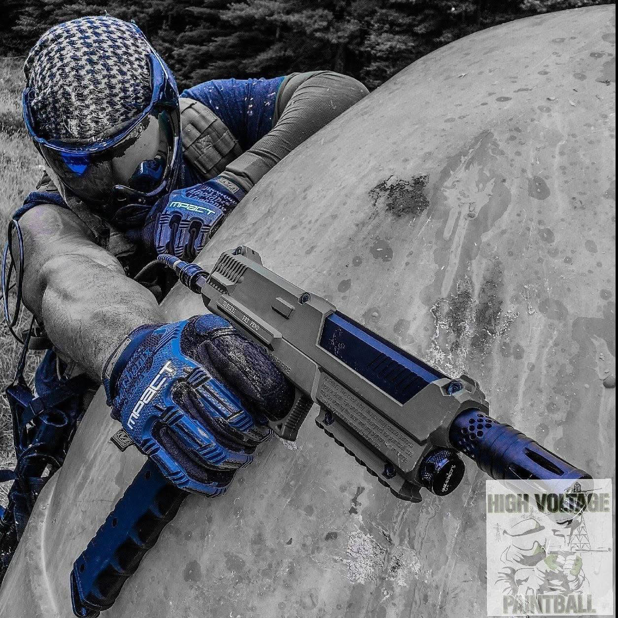 Jugador apuntando con un marcador de paintball junto a una gran roca durante una partida en High Voltage Paintball.
