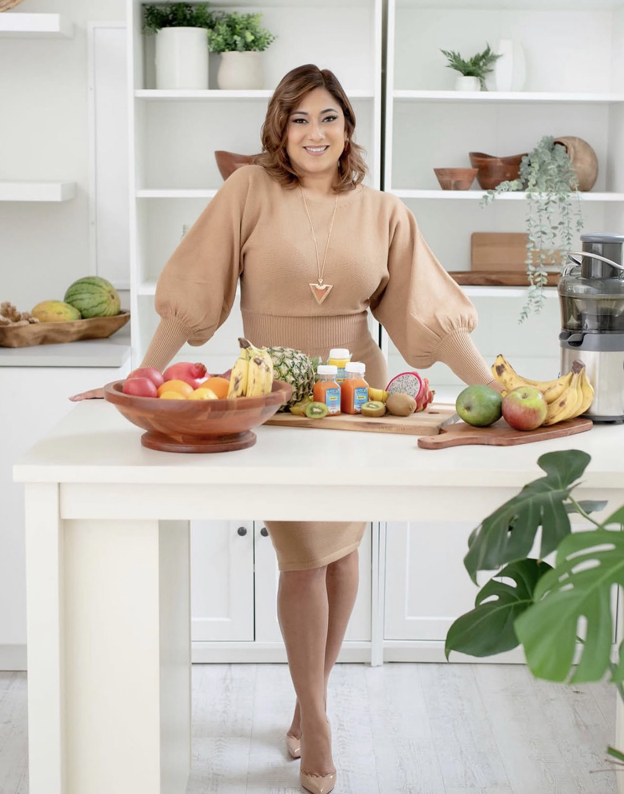 Helayne Jobson standing at a kitchen island, with fresh fruit and Juice Conmigo bottles.