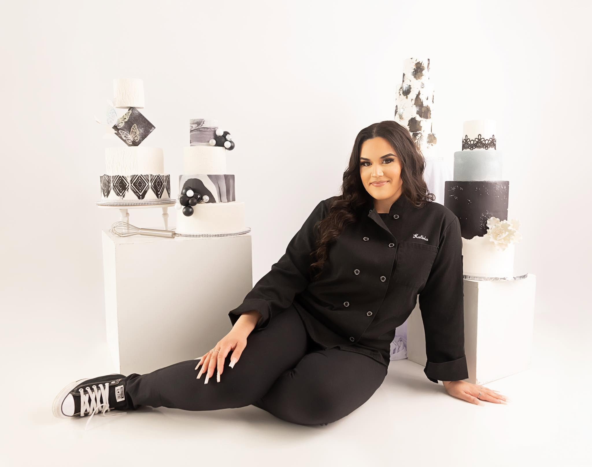 Katiria Andujar, con su chaqueta de chef bordada con su nombre, junto a varios de sus cakes de boda de varios niveles.