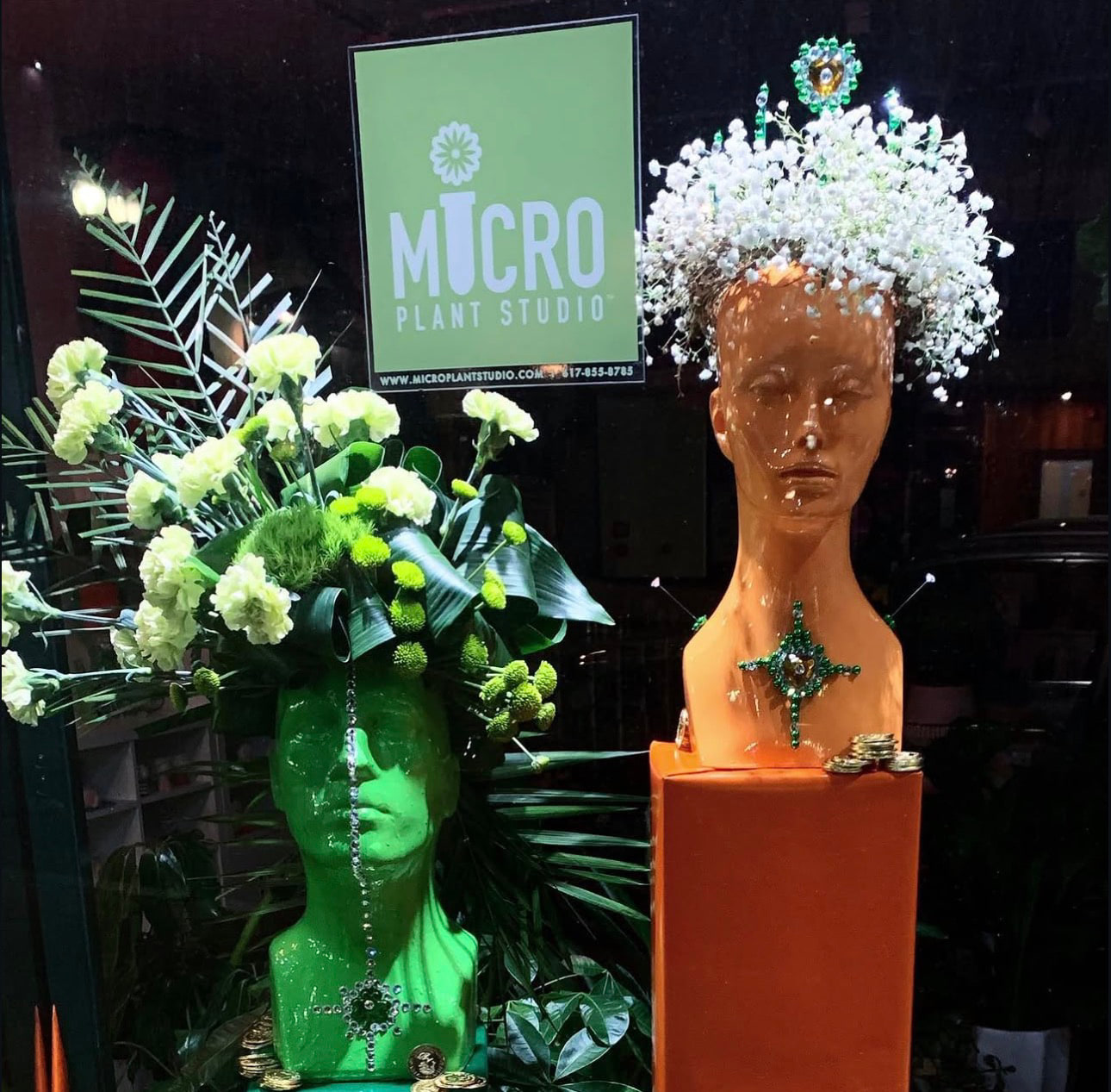 Escaparate de Micro Plant Studio: dos cabezas de maniquí adornadas con flores junto al letrero del estudio.
