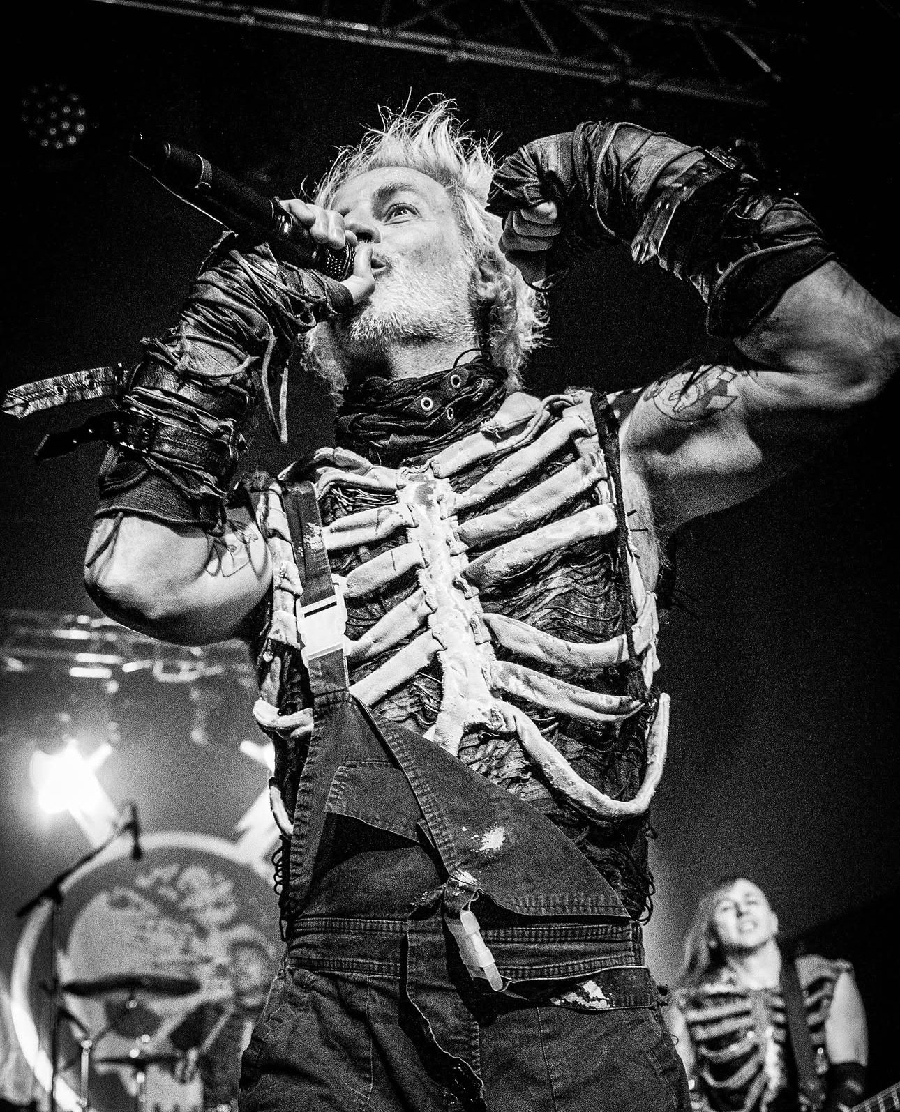 Vocalista con chaleco de esqueleto cantando al micrófono, en blanco y negro