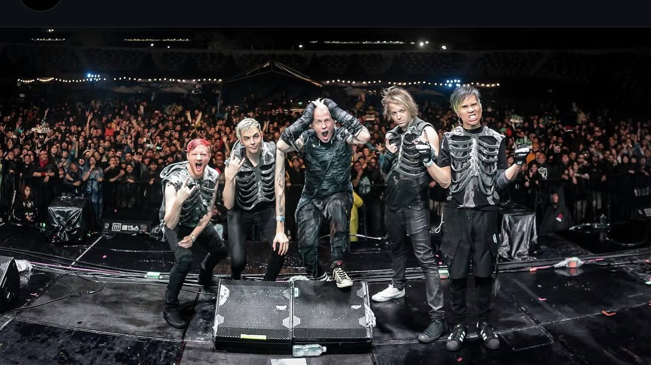 Cinco integrantes de Powerman 5000 con chalecos de esqueleto, al borde del escenario frente a una multitud