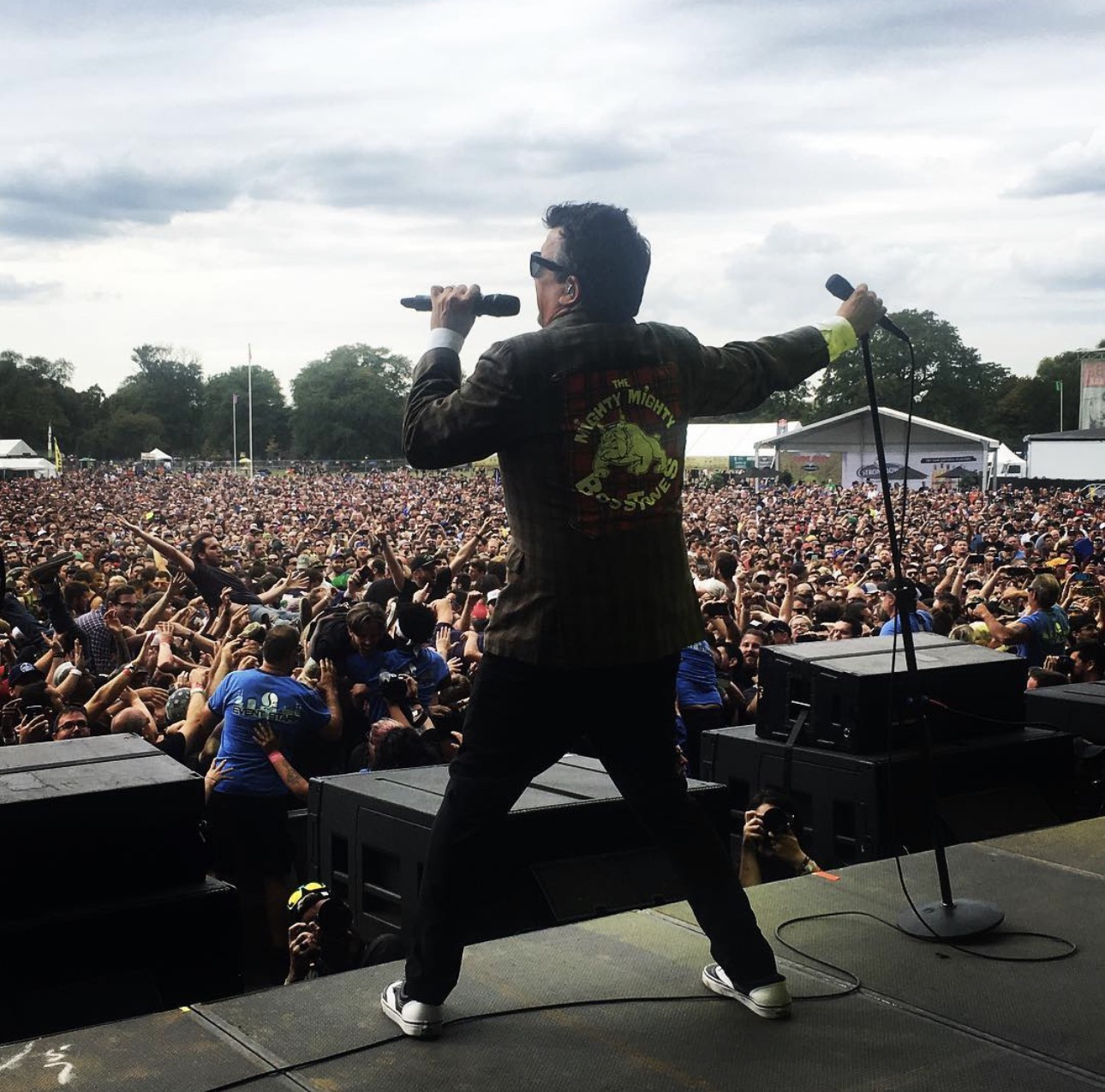 Un integrante de la banda, de espaldas, con la chaqueta con el logo del bulldog de The Mighty Mighty Bosstones, frente a una multitud en un festival